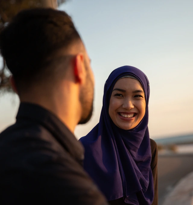 two people talking. The woman facing the camera is wearign a hijab and smiling.